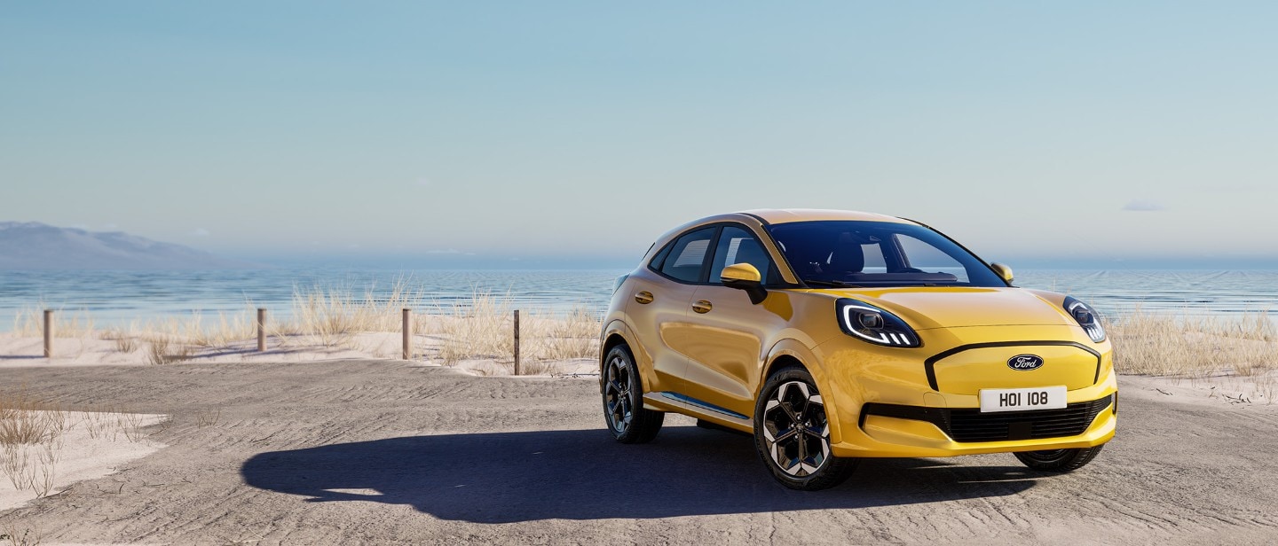Een gele Elektrische Ford Puma Gen-E staat geparkeerd met op de achtergrond de zee