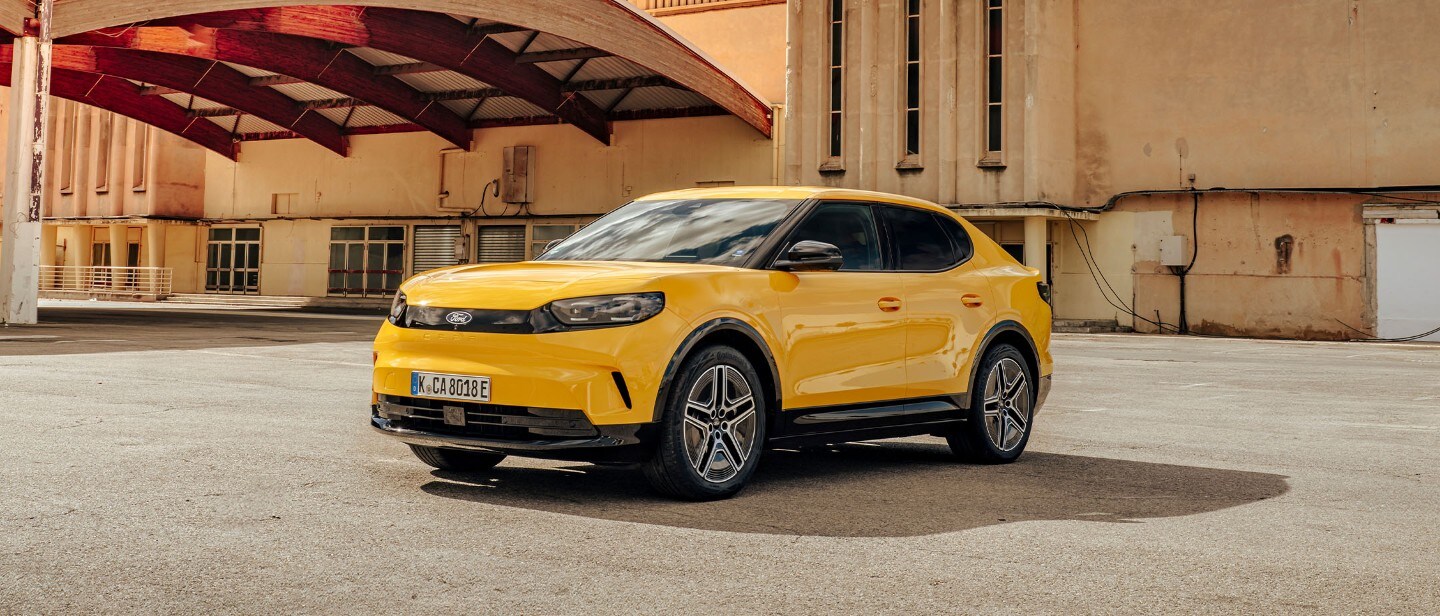 Brede opname van de volledig elektrische Ford Capri (geel) geparkeerd voor een pand.