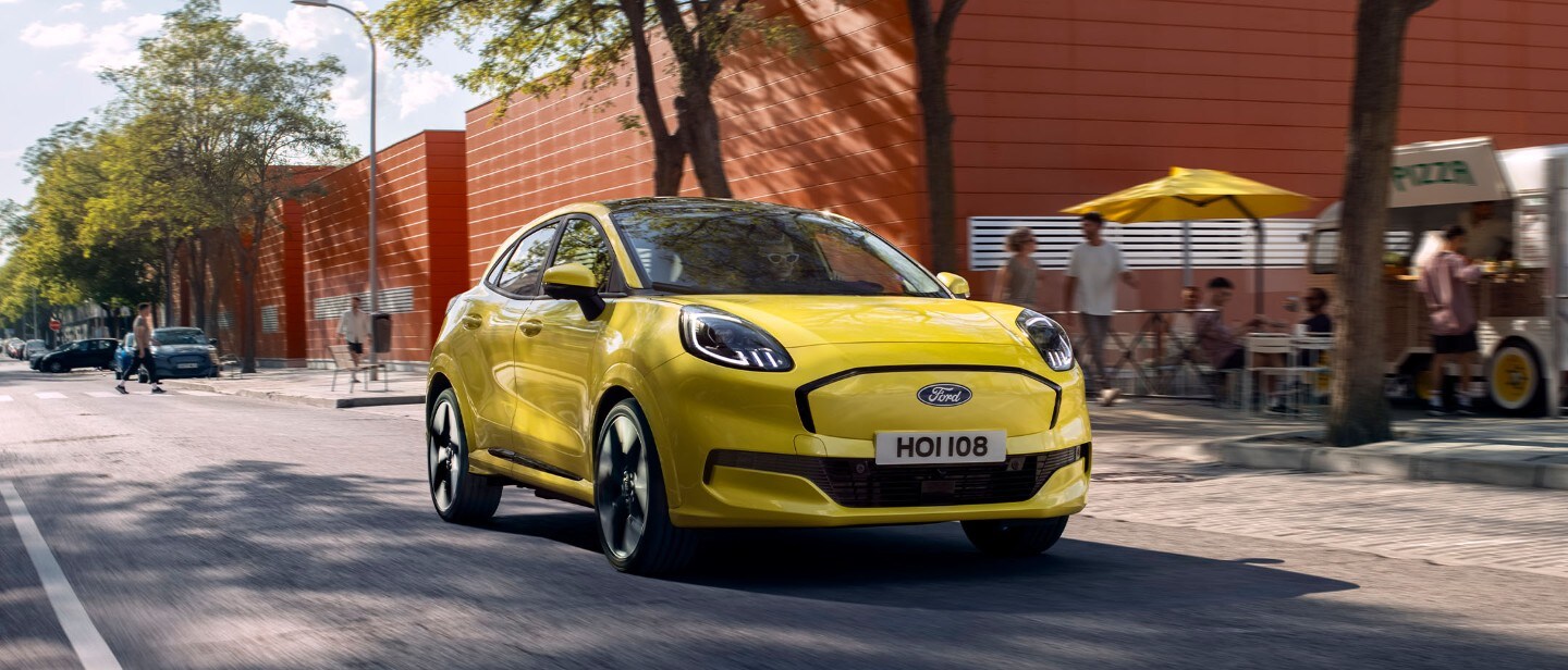 Brede opname van een nieuwe volledig elektrische Ford Puma Gen-E (geel) op de open weg in de stad.
