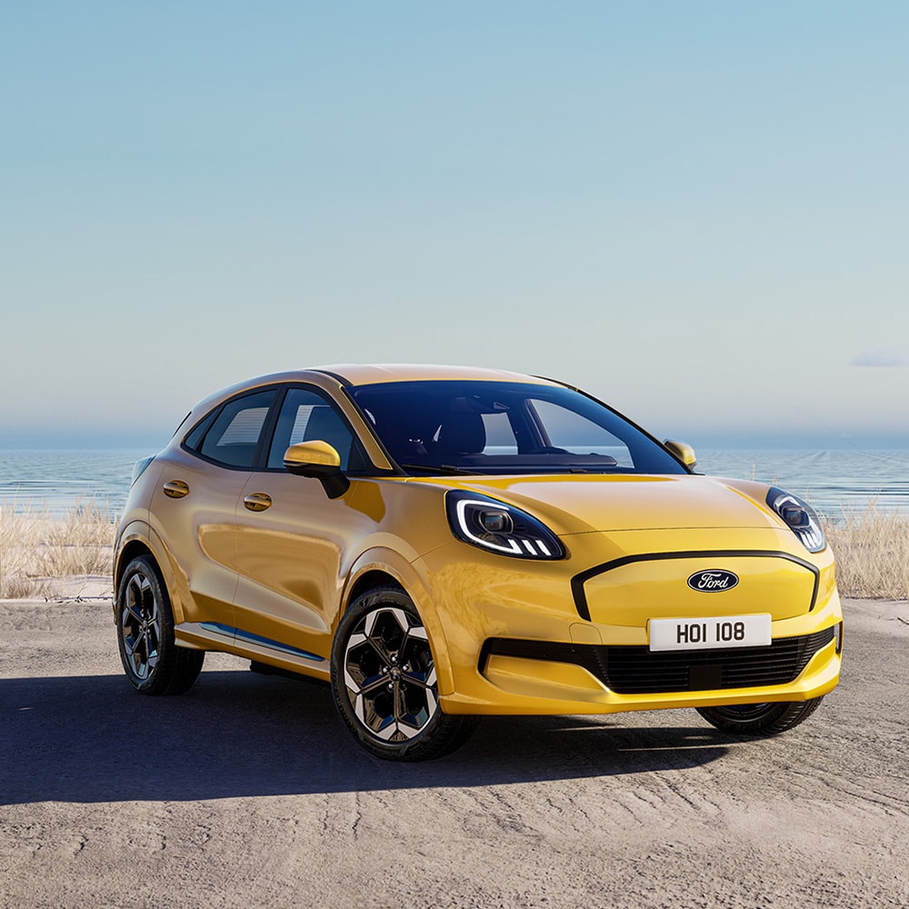 Een gele Elektrische Ford Puma Gen-E staat geparkeerd met op de achtergrond de zee