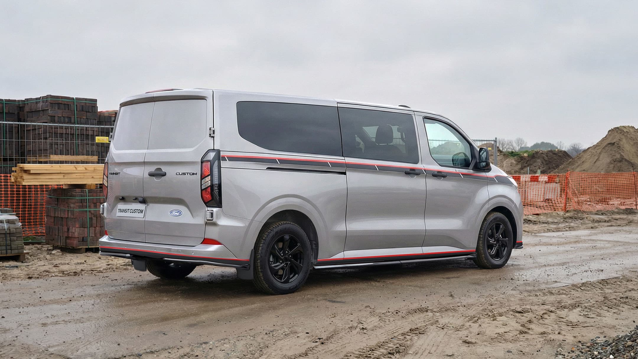 Achterraanzicht van de Ford Transit Custom PHEV Grey Platinum, en staat geparkeerd op een bouwterrein 