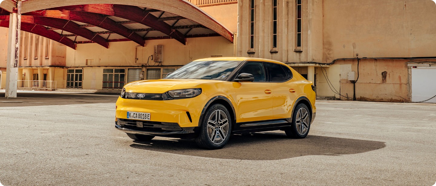 Brede opname van de volledig elektrische Ford Capri (geel) geparkeerd voor een pand.
