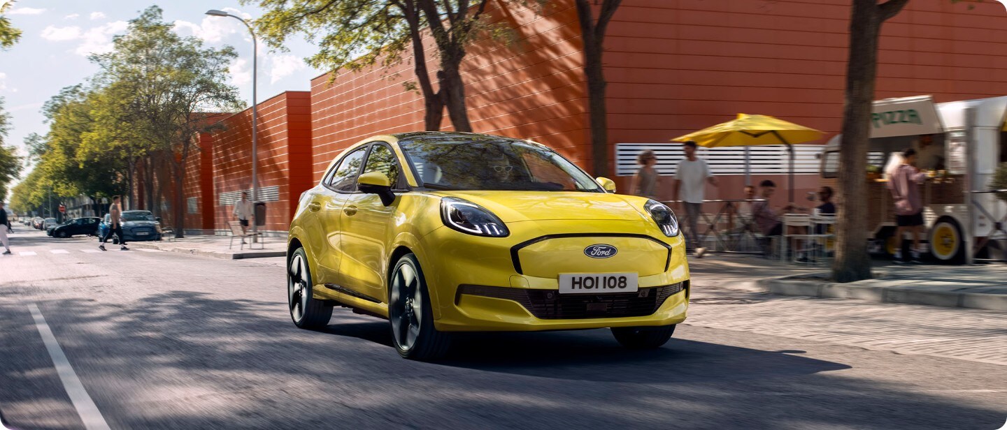 Brede opname van een nieuwe volledig elektrische Ford Puma Gen-E (geel) op de open weg in de stad.