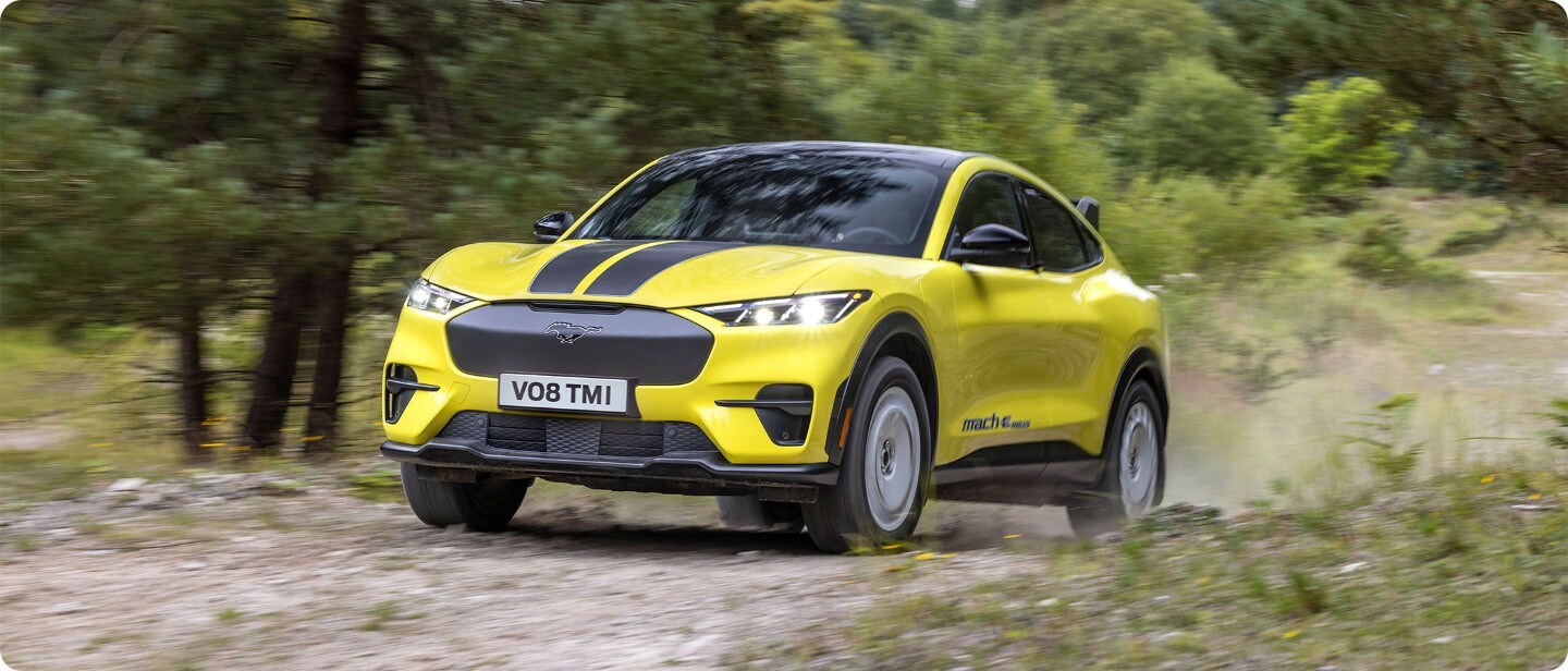 Brede opname van een volledig elektrische Ford Mustang Mach-e Rally (geel) die door de bossen rijd.