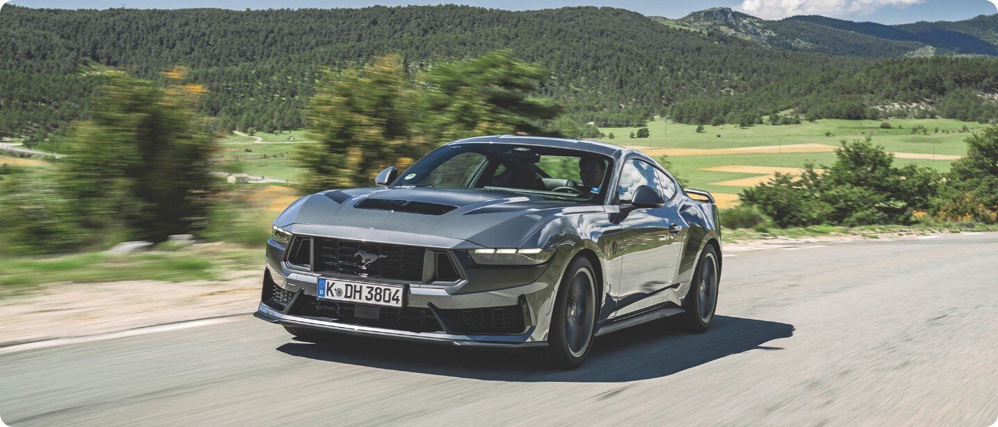 Brede opname van een Ford Mustang Dark Horse (grijs) die op de open weg rijd.