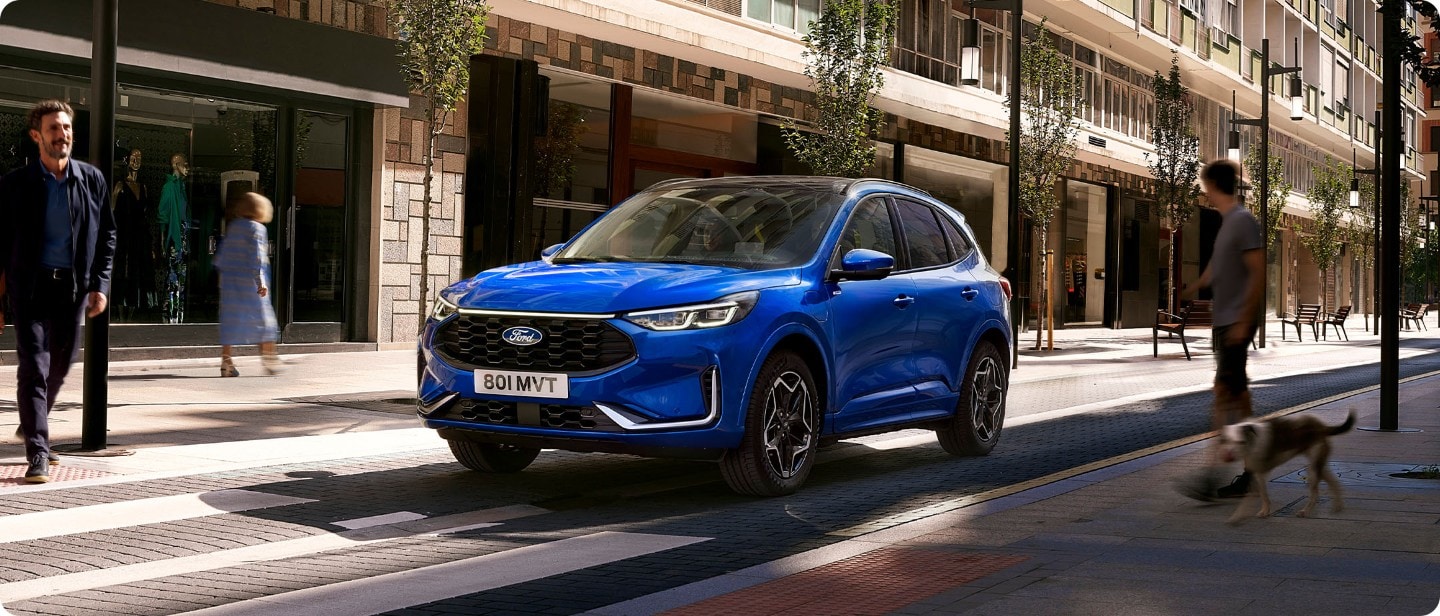 Brede opname van de Ford Kuga (blauw) stilstaand voor een zebrapad.