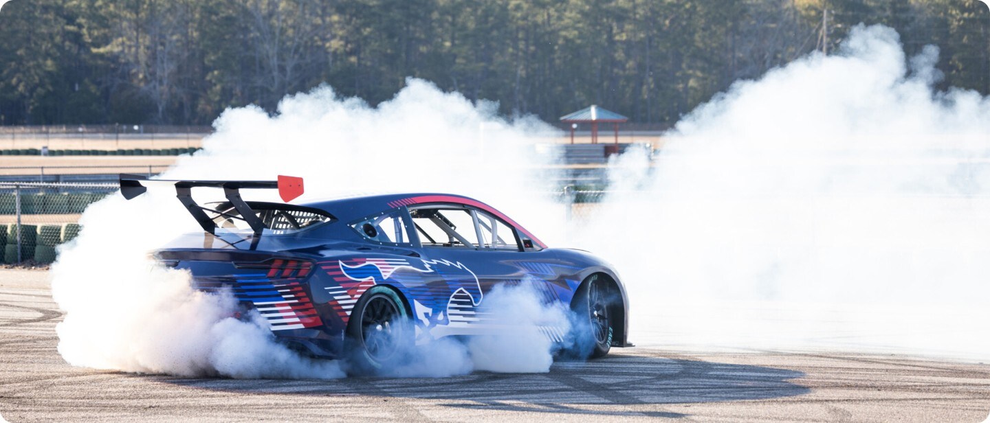 Brede opname van de Ford Mustang Mach-e Performance(blauw) driftend op een parkeerplaats.