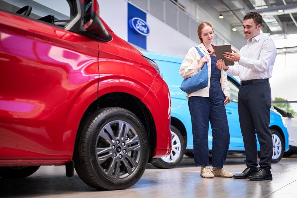Een medewerker van de showroom bekijkt samen met een klant informatie op een tablet naast een rode bus.