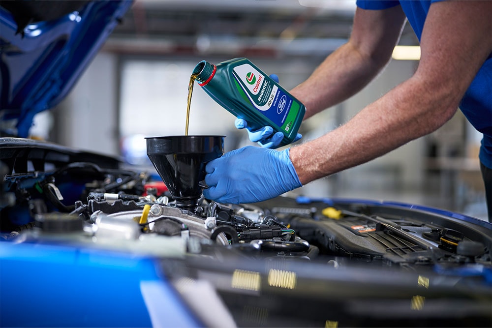 Motorolie van Castrol wordt via een trechter in de motor van een blauwe auto gegoten.
