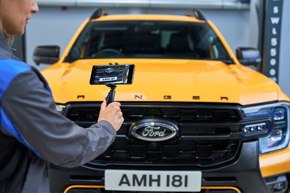 Een monteur maakt een video van de grille van een gele Ford Ranger met een smartphone.