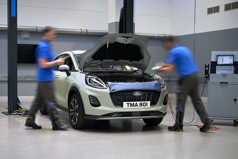 Twee monteurs werken aan een witte Ford Puma met de motorkap open in een servicewerkplaats.