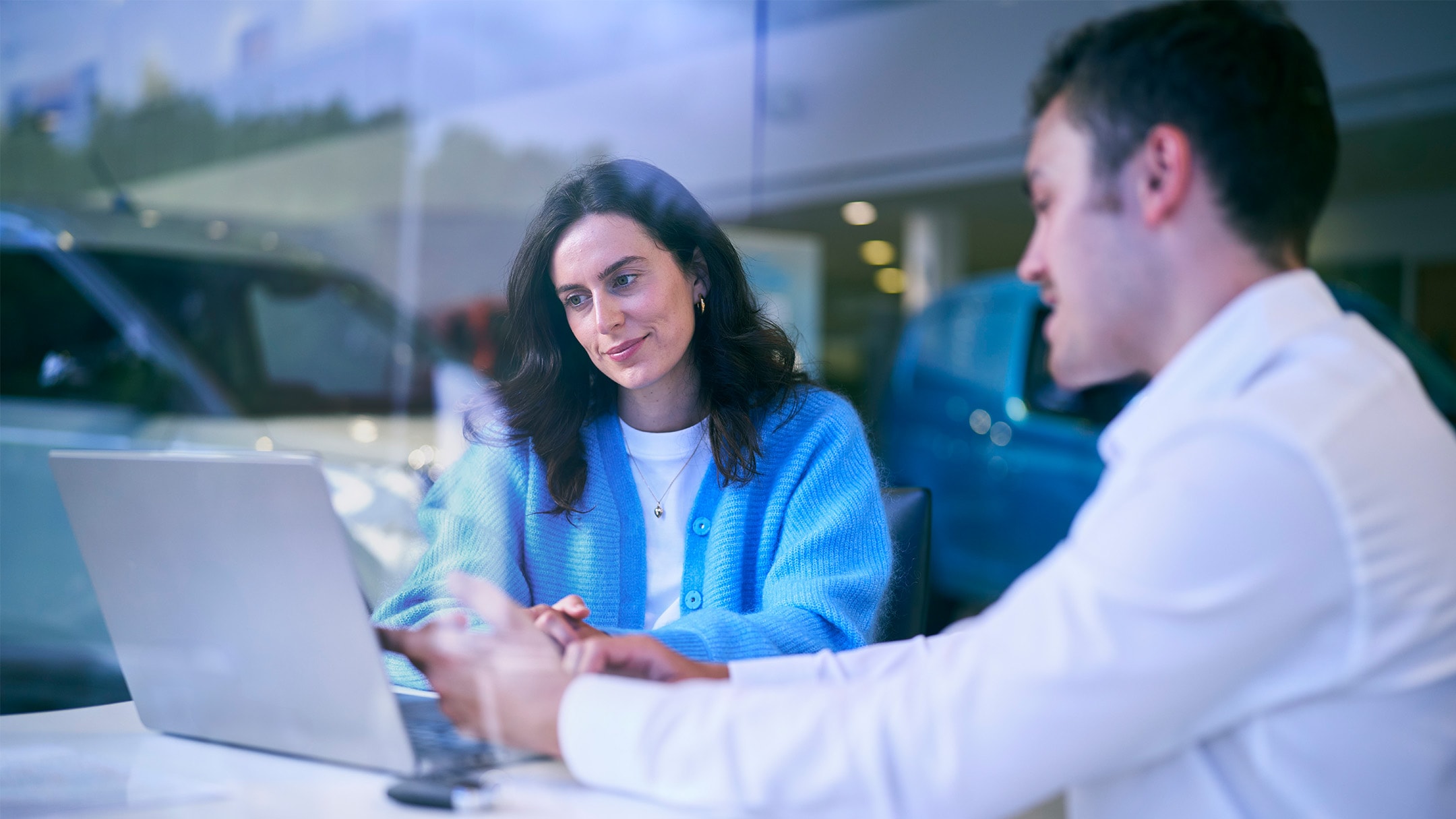 Twee personen in gesprek aan een tafel met een laptop, op de achtergrond is een Ford-voertuig zichtbaar.