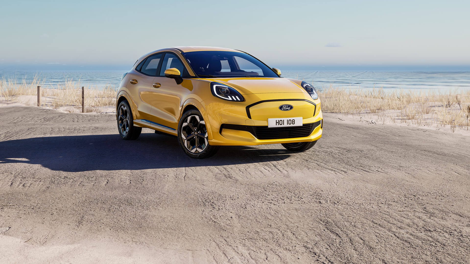 Een gele Elektrische Ford Puma Gen-E staat geparkeerd met op de achtergrond de zee