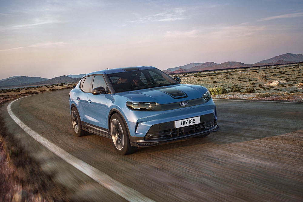 Vooraanzicht van een blauwe Ford Capri die op een kronkelende weg rijdt.