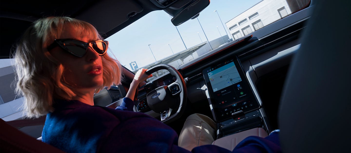 Een vrouw zit in de bestuurdersstoel van de elektrische Ford Capri. Tevens is het grote 14,6" SYNC Move-touchscreen te zien.