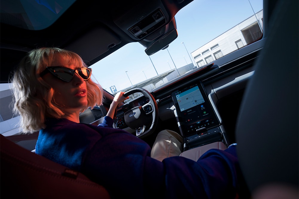 Een vrouw zit in de bestuurdersstoel van de elektrische Ford Capri. Tevens is het grote 14,6" SYNC Move-touchscreen te zien.