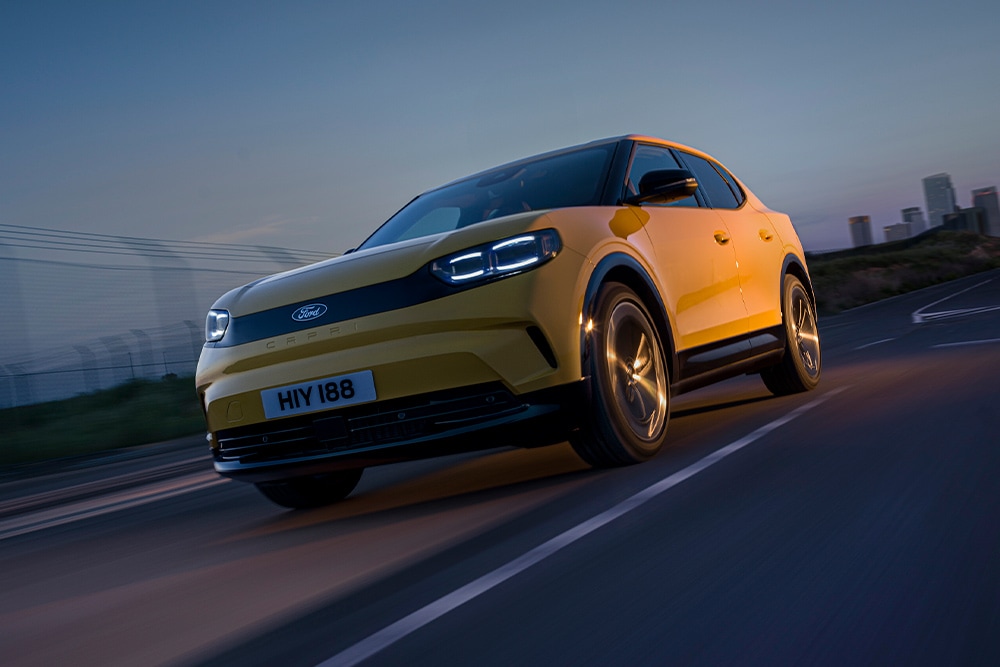 A yellow Ford Capri electric car driving along an open road. 
