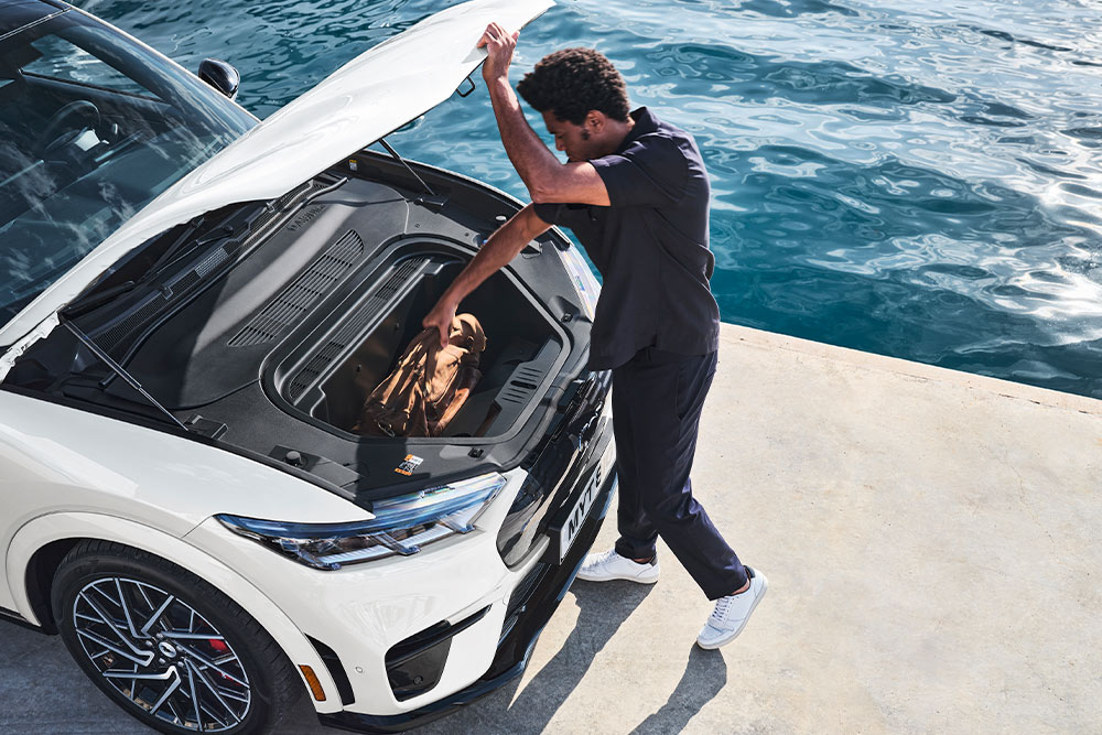 A person placing a holdall bag into the frunk of a white Ford Mustang Mach-E electric car. 