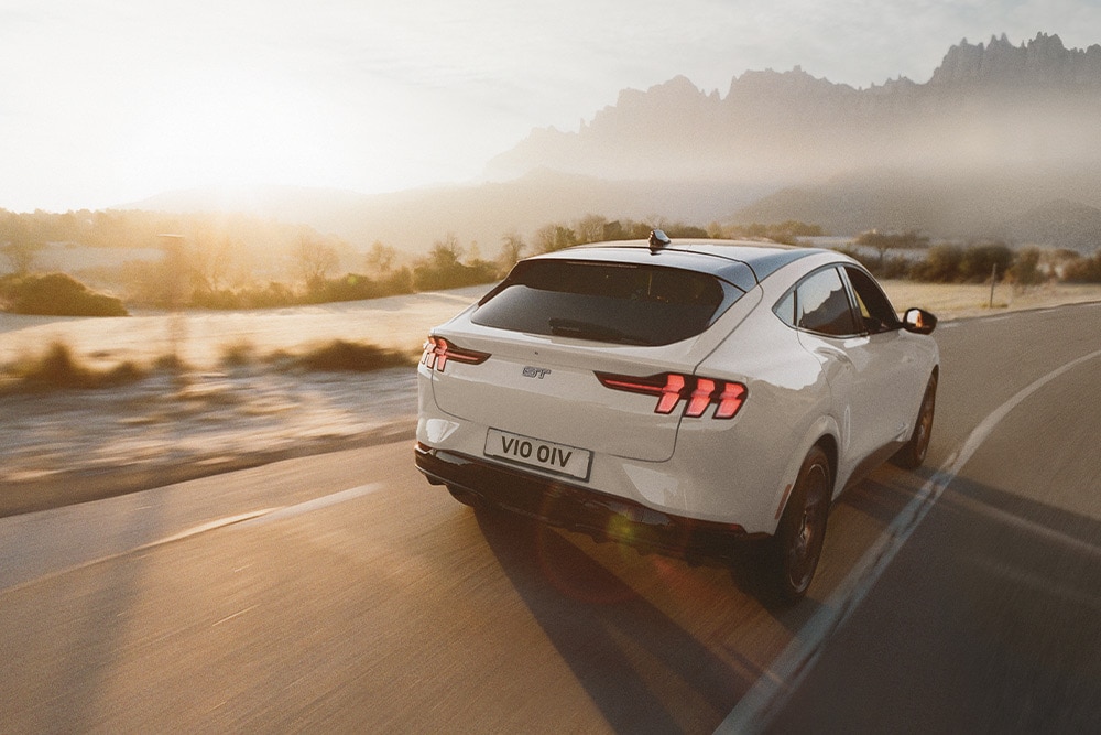 A silver electric Ford Mustang Mach-E GT driving along a scenic road.