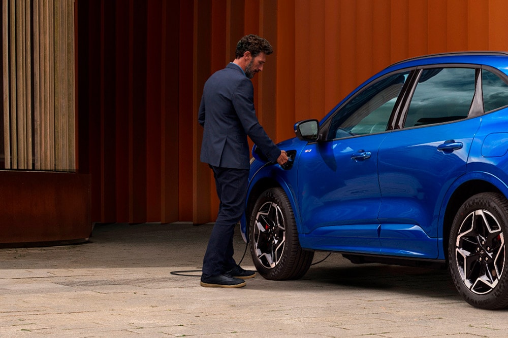 A person plugging an EV home charging cable into a Ford plug-in hybrid car.
