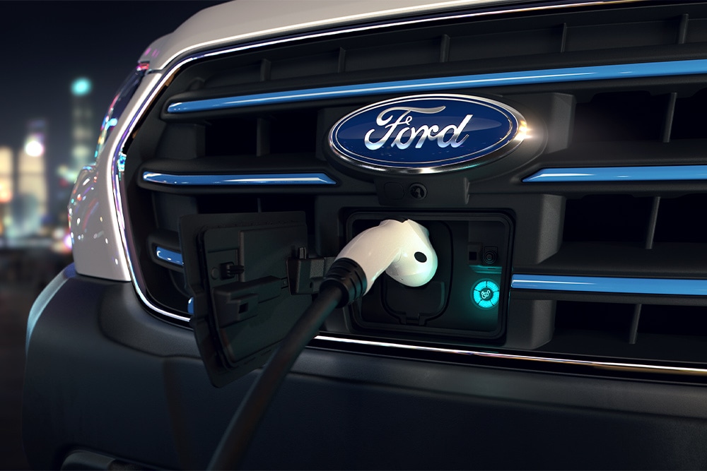 Close-up of an Ford E-Transit van charging point and blue oval Ford badge on the front grille. 