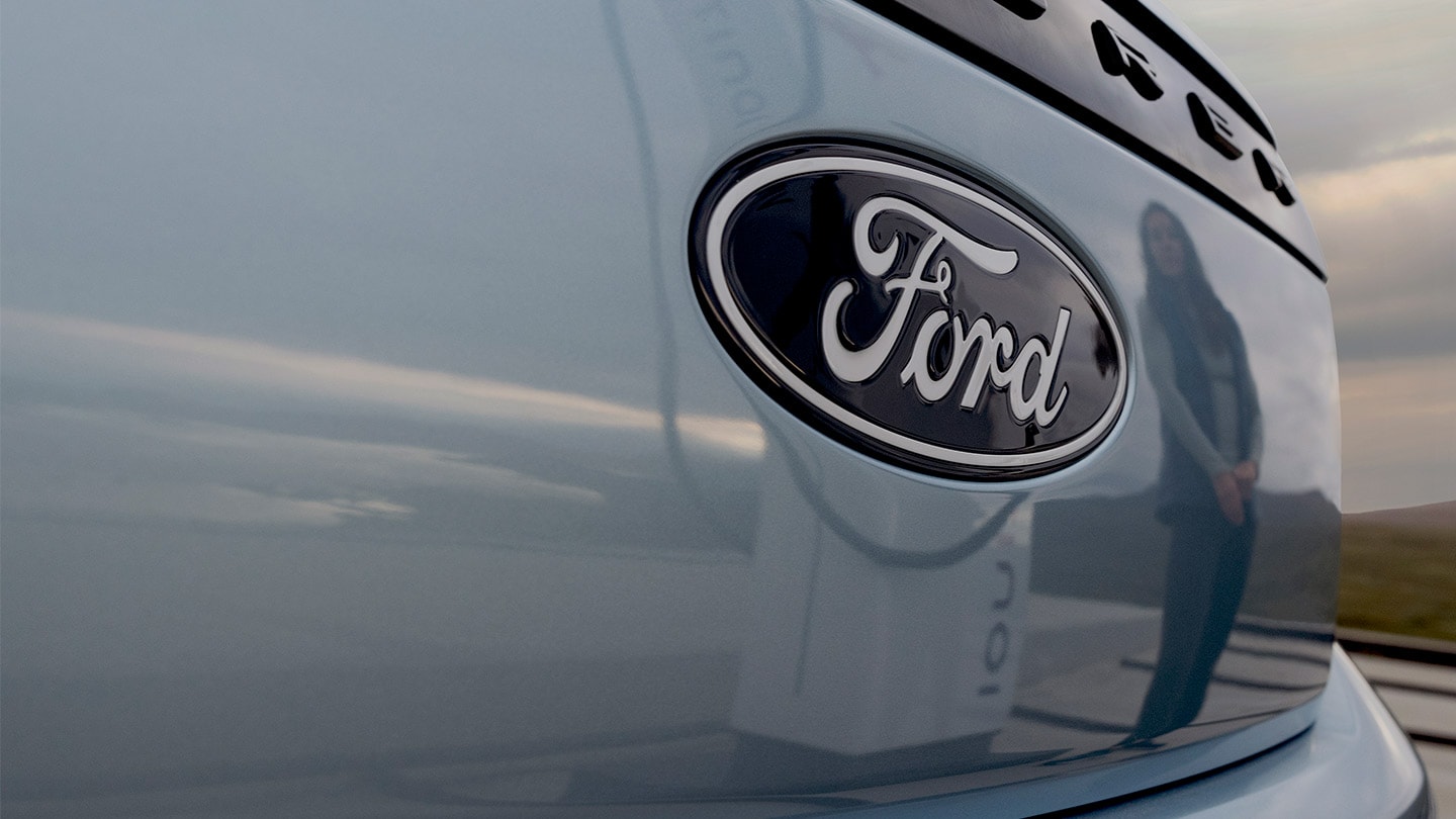 Ford logo on a blue electric Ford Explorer with a public charging station reflected in the car.