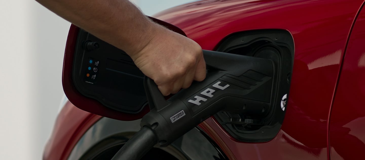 Close-up of a red Ford EV being connected to a public HPC (High Power Charger), for fast public EV charging.