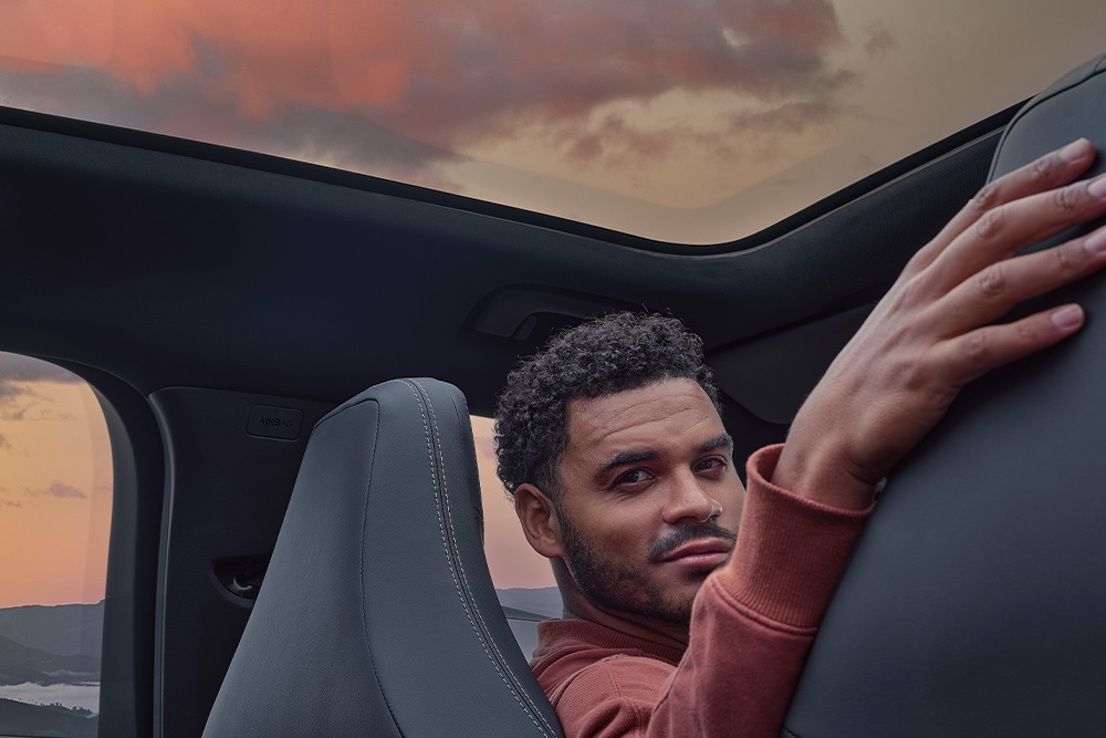 Een man zit bij zonsondergang in een auto met zijn hand op de rugleuning van een van de stoelen.