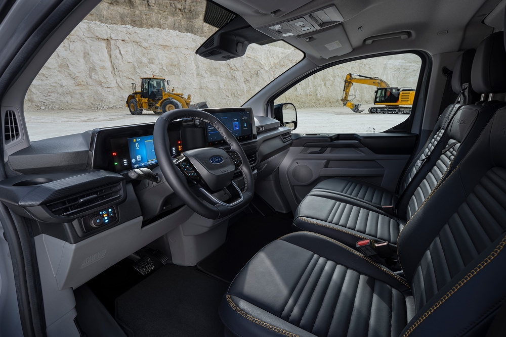 Het interieur van een elektrische Ford E-Transit Custom-bestelwagen, met de stoelen en het stuur, geparkeerd in een steengroeve. 