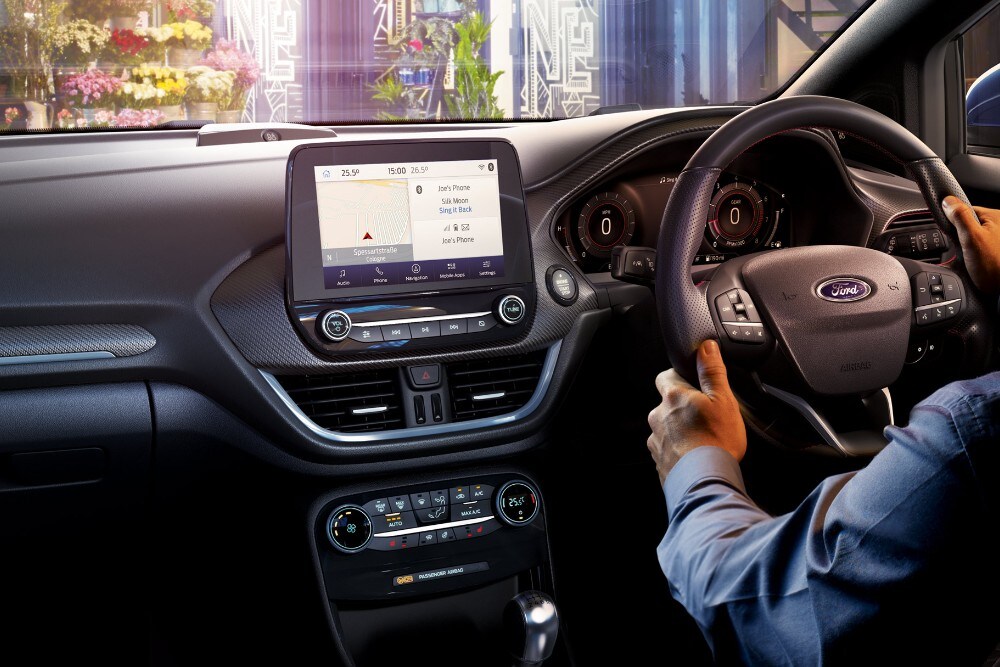 Interior of a Ford Puma with a person's hands on the steering wheel and a large touchscreen display.