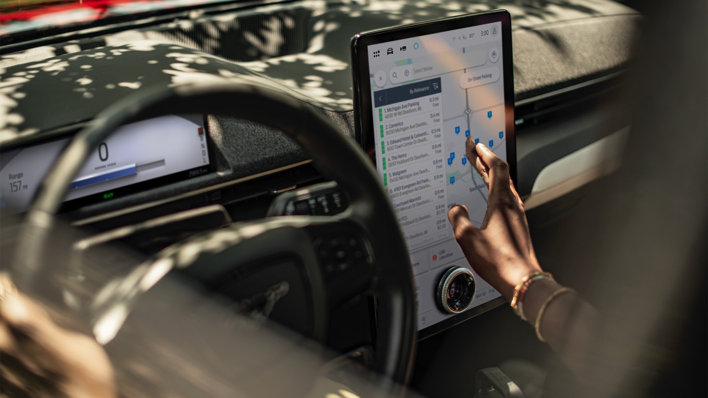 Een close-up van een vrouw in een Ford Mustang Mach-E die het grote SYNC-touchscreen gebruikt.