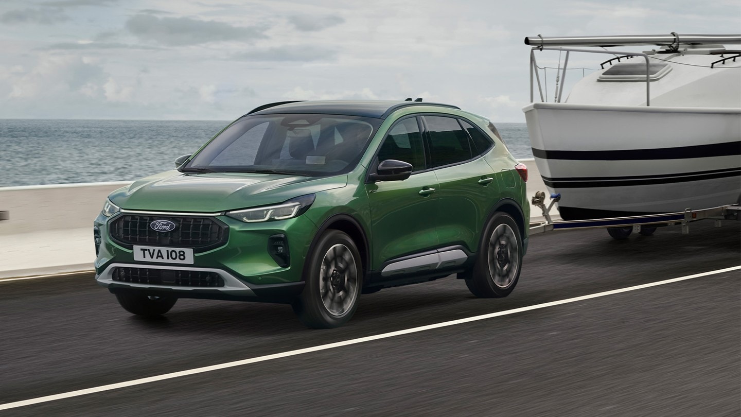 Een groene Ford Kuga die een kleine boot trekt langs een kustweg.