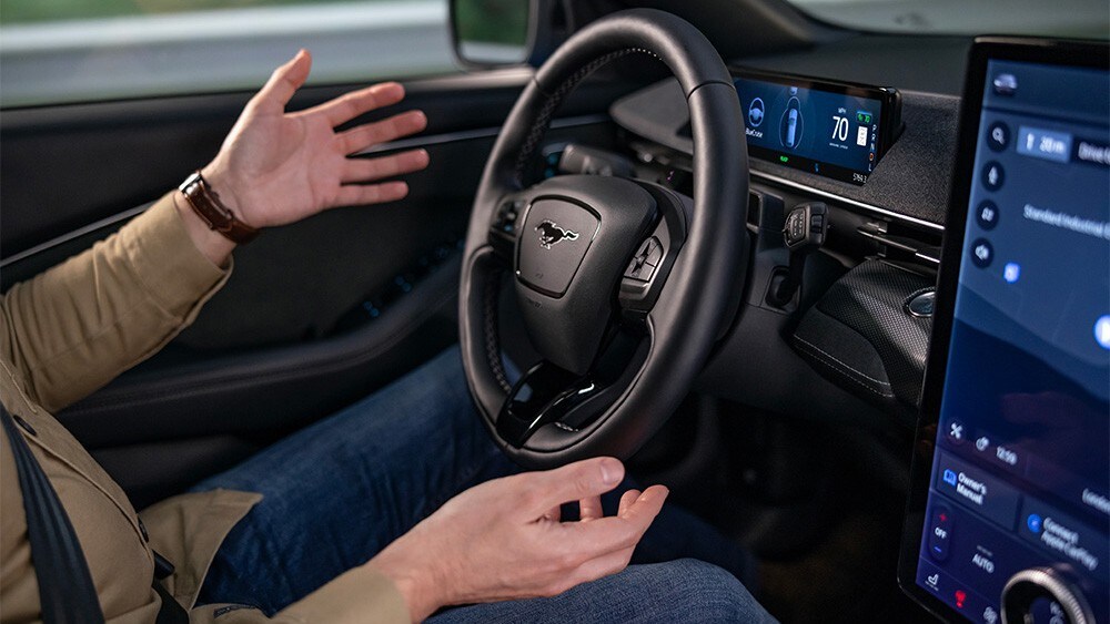 Een man zit in de Ford Mustang Mach-E met zijn handen los van het stuur, om de BlueCruise-technologie te laten zien.