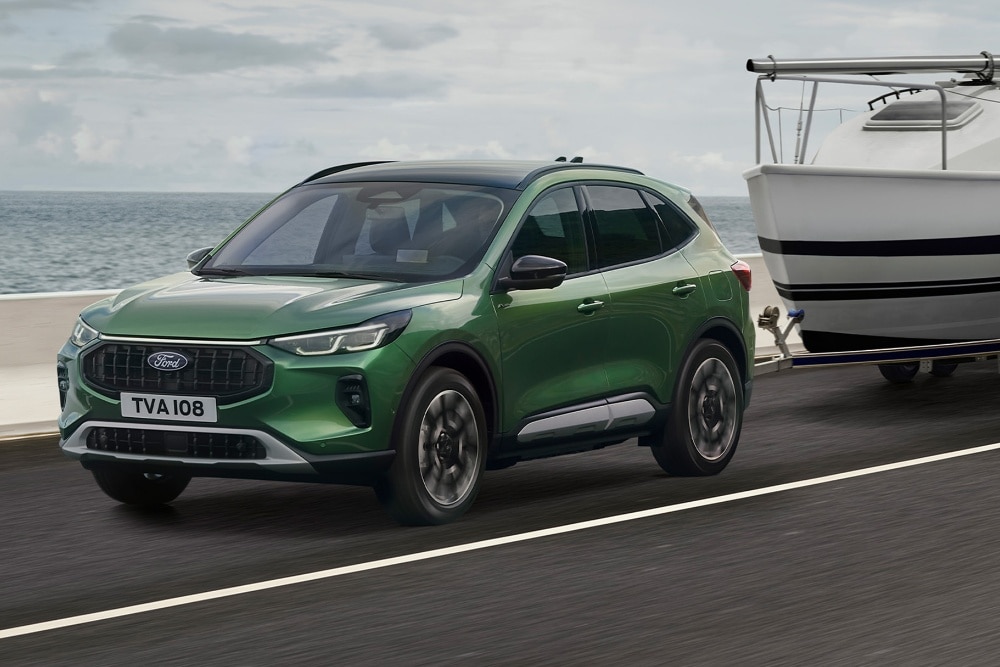 Een groene Ford Kuga die een kleine boot trekt langs een kustweg.