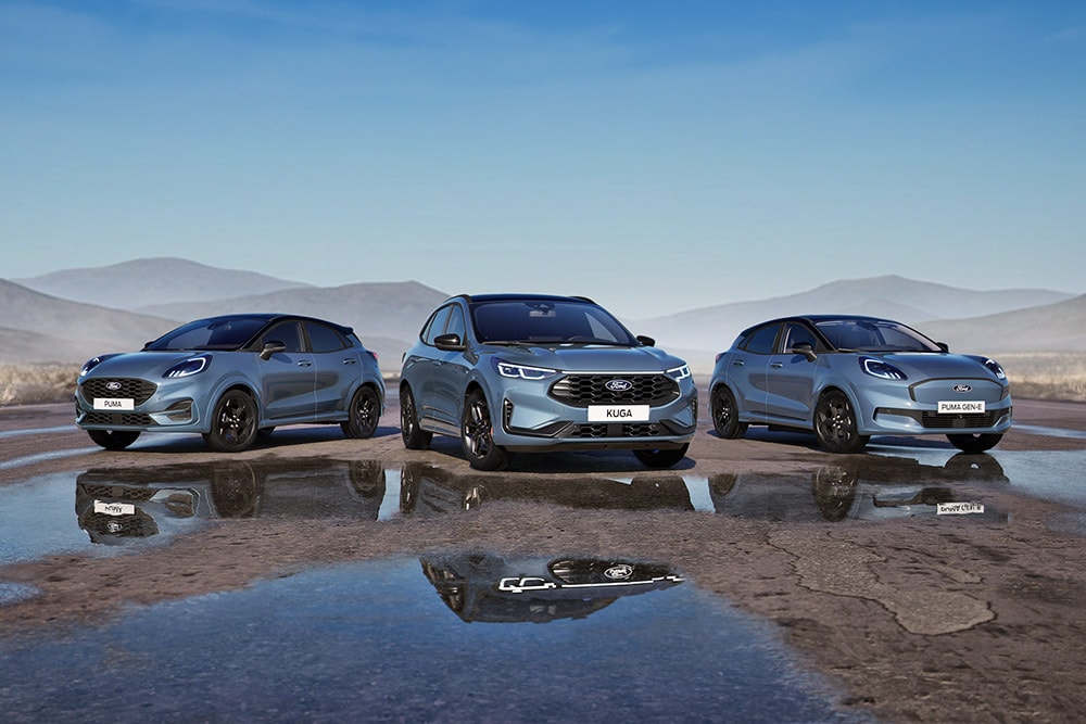 Een Ford Puma, Ford Kuga en Ford Puma Gen-E staan geparkeerd op een natte weg met bergen op de achtergrond.