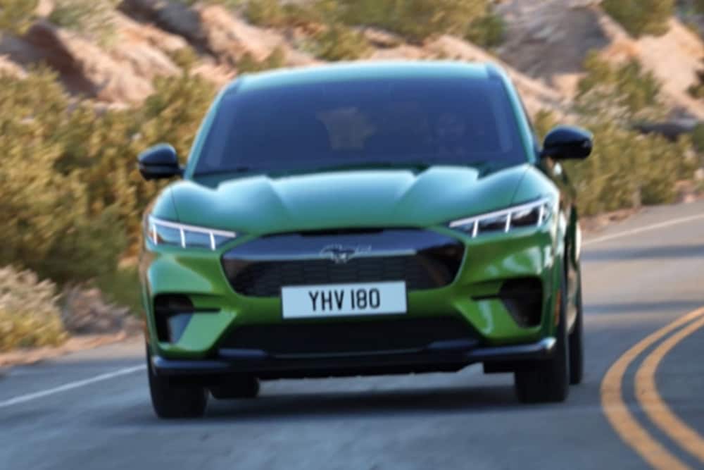 Vooraanzicht van een groene Ford Mustang Mach-E die over een bergweg rijdt.