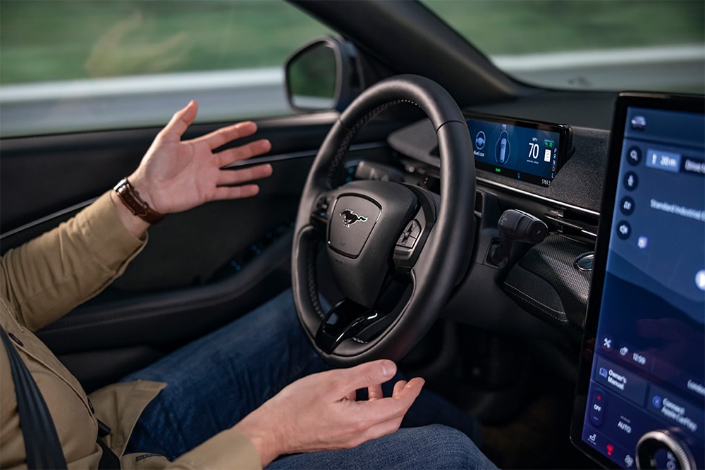 Twee handen zweven bij het stuur van de Mustang Mach-E om de BlueCruise-technologie voor autonoom rijden te demonstreren.