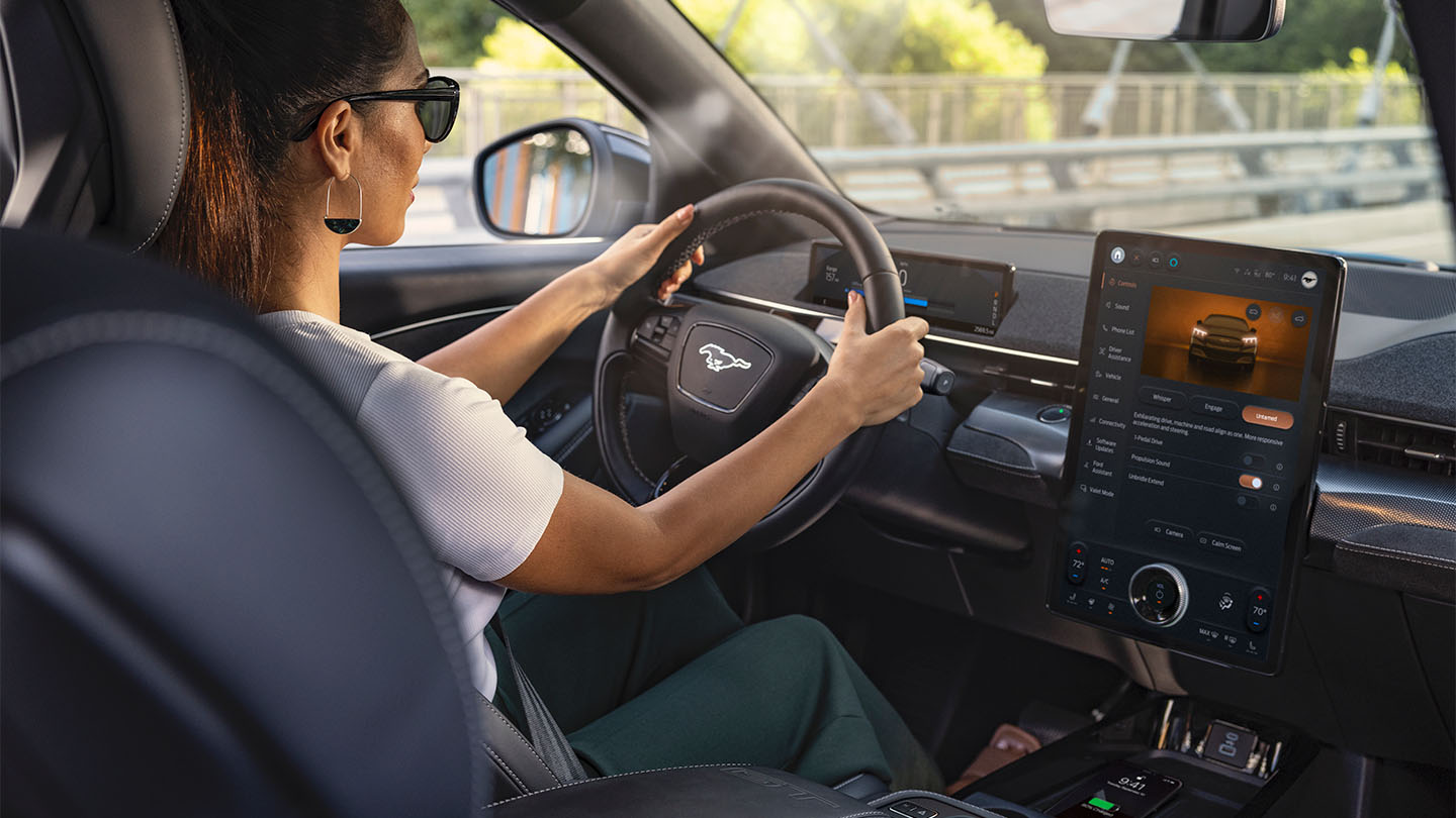 Een vrouw rijdt in de Mustang Mach-E met haar handen aan het stuur. Op het 15,5" touchscreen zie je details over de auto.
