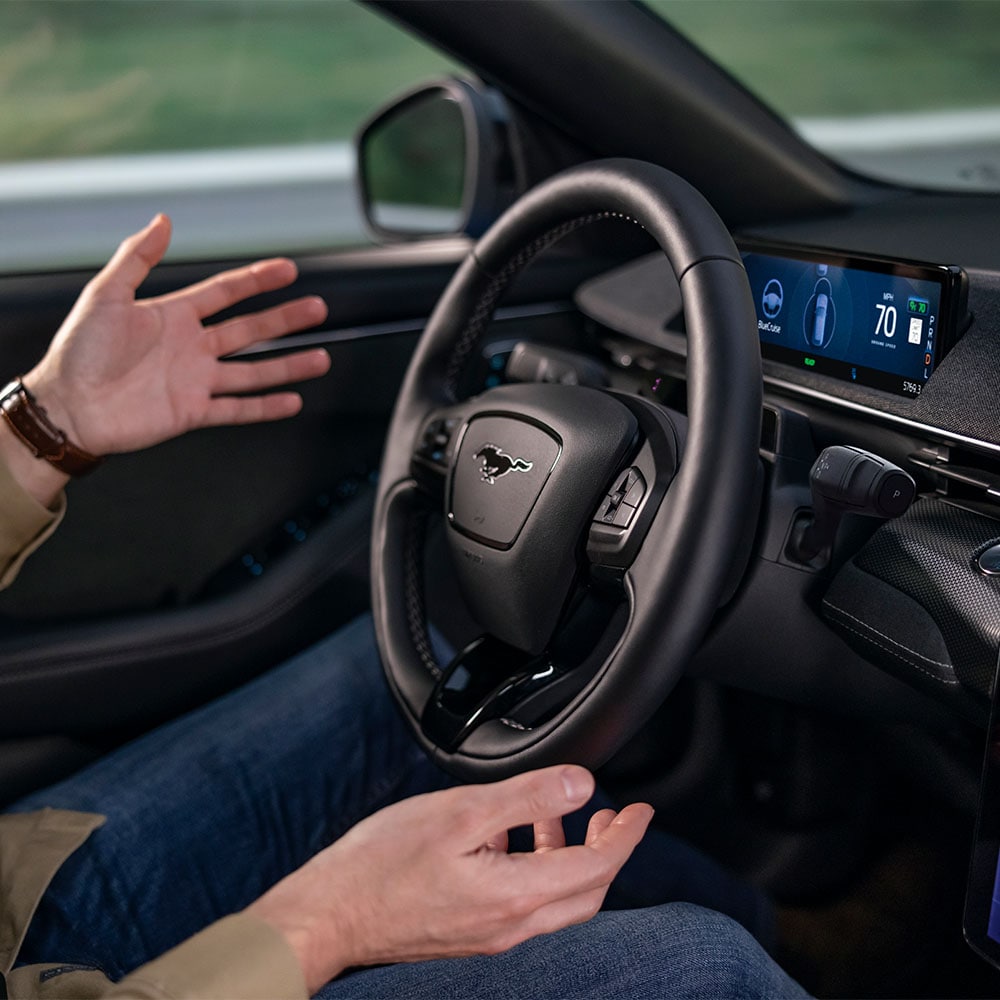 Twee handen zweven bij het stuur van de Mustang Mach-E om de BlueCruise-technologie voor autonoom rijden te demonstreren.