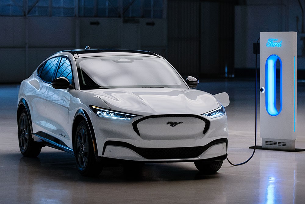 Een witte Ford Mustang Mach-E die is aangesloten op een Ford-laadstation in een moderne garage.