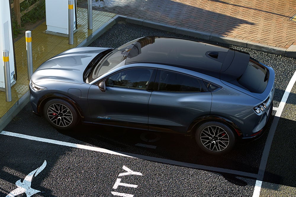 Bovenaanzicht van een grijze Ford Mustang Mach-E geparkeerd op een parkeerplaats met laadpunten.