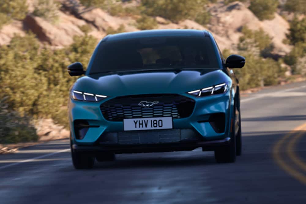 Vooraanzicht van een blauwe Ford Mustang Mach-E die op een bergweg rijdt.