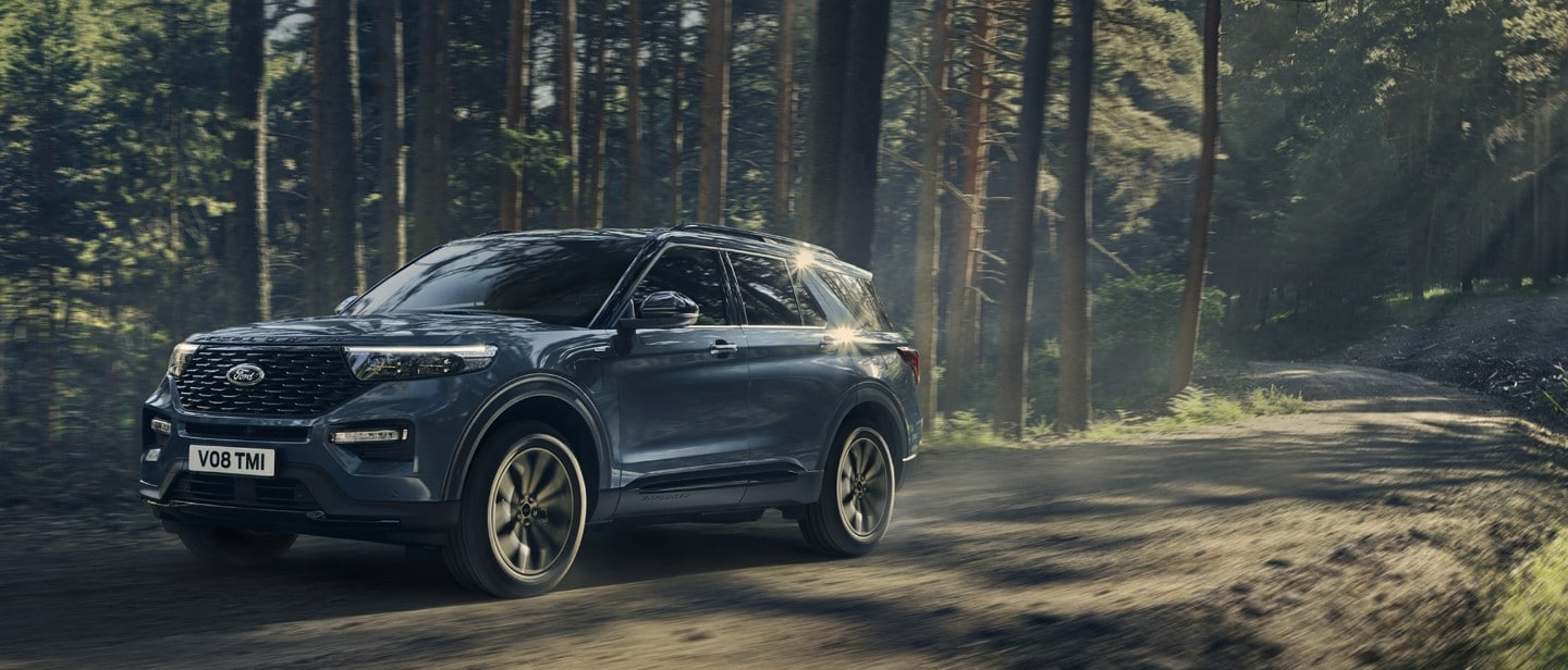 New metallic blue Ford Explorer PHEV in motion driving through forest