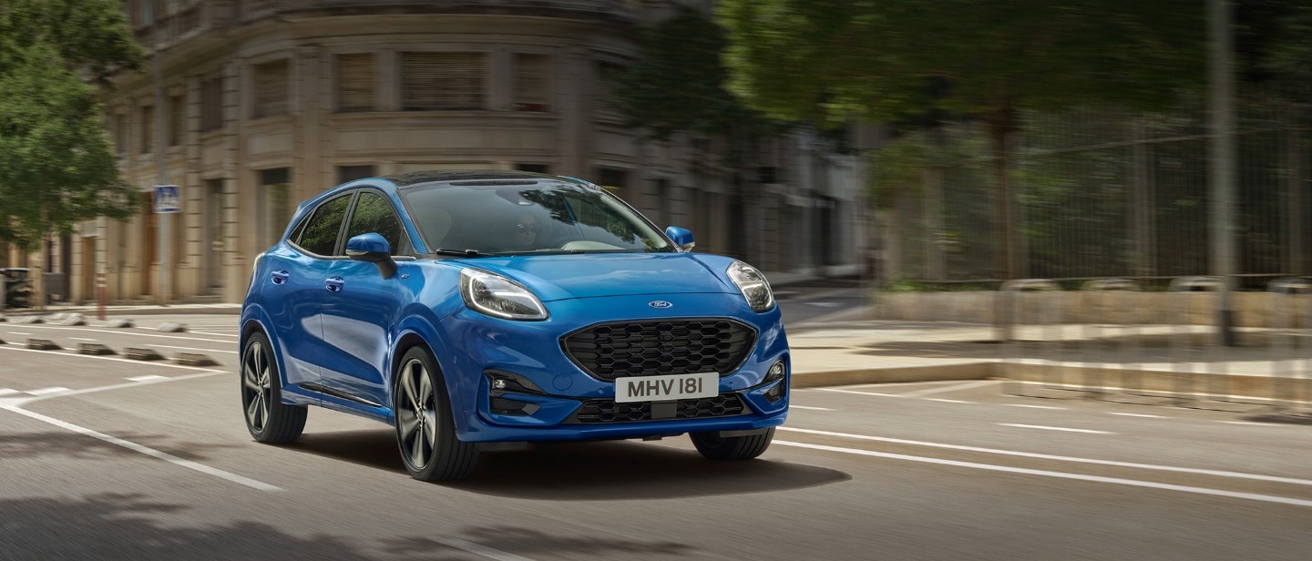 New Blue Ford Puma driving in city with trees behind