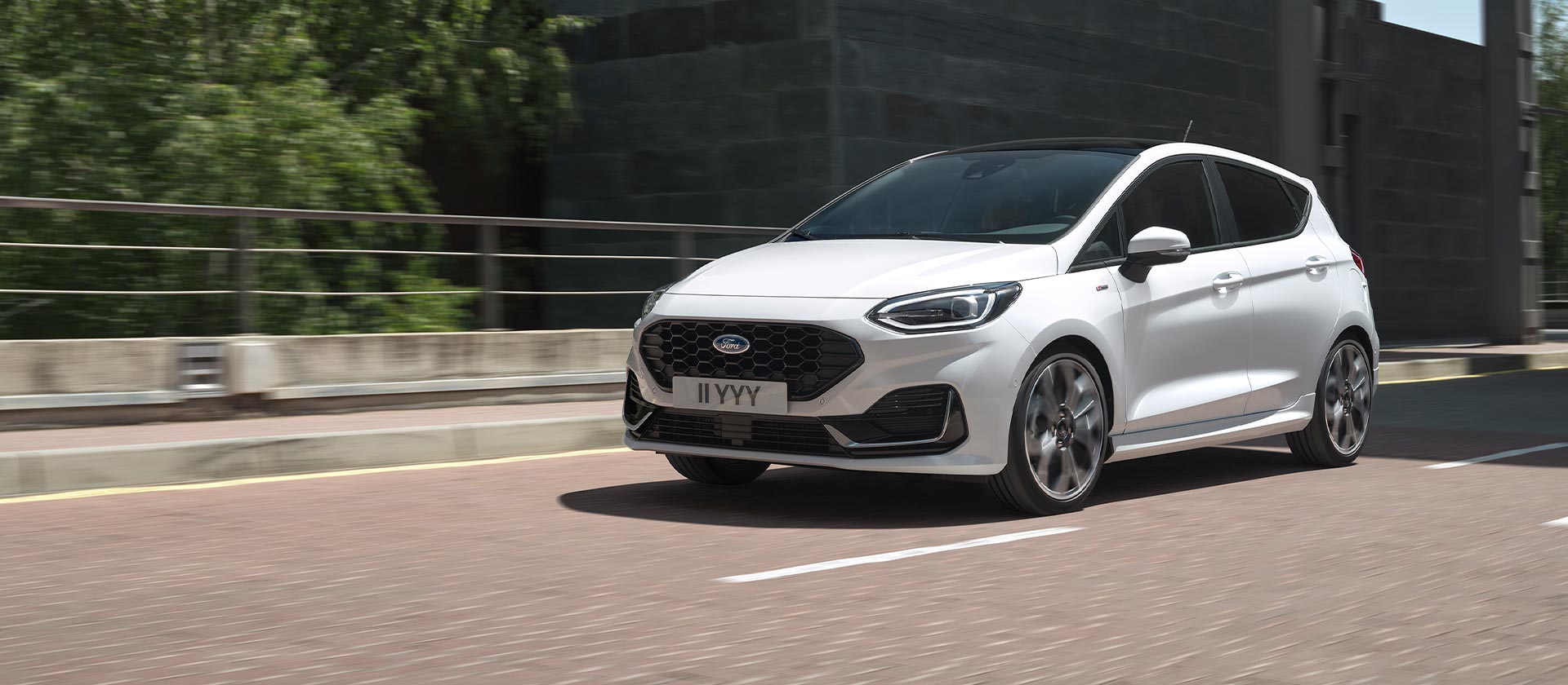 Witte Ford Fiesta die door een drukke binnenstad rijdt.