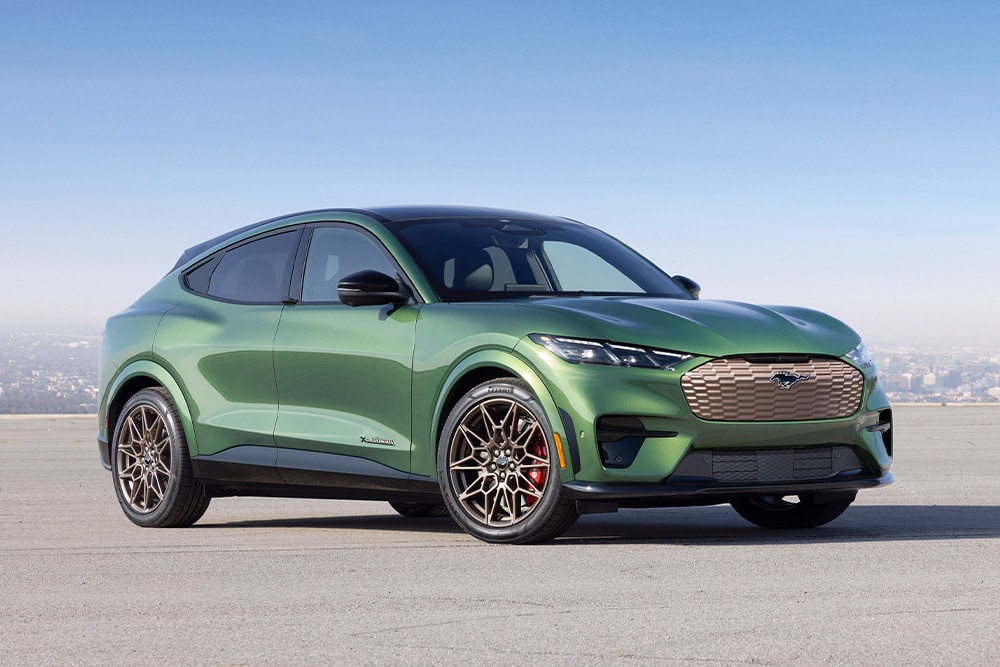 Groene Ford Mustang Mach‑E geparkeerd voor een stadslandschap.