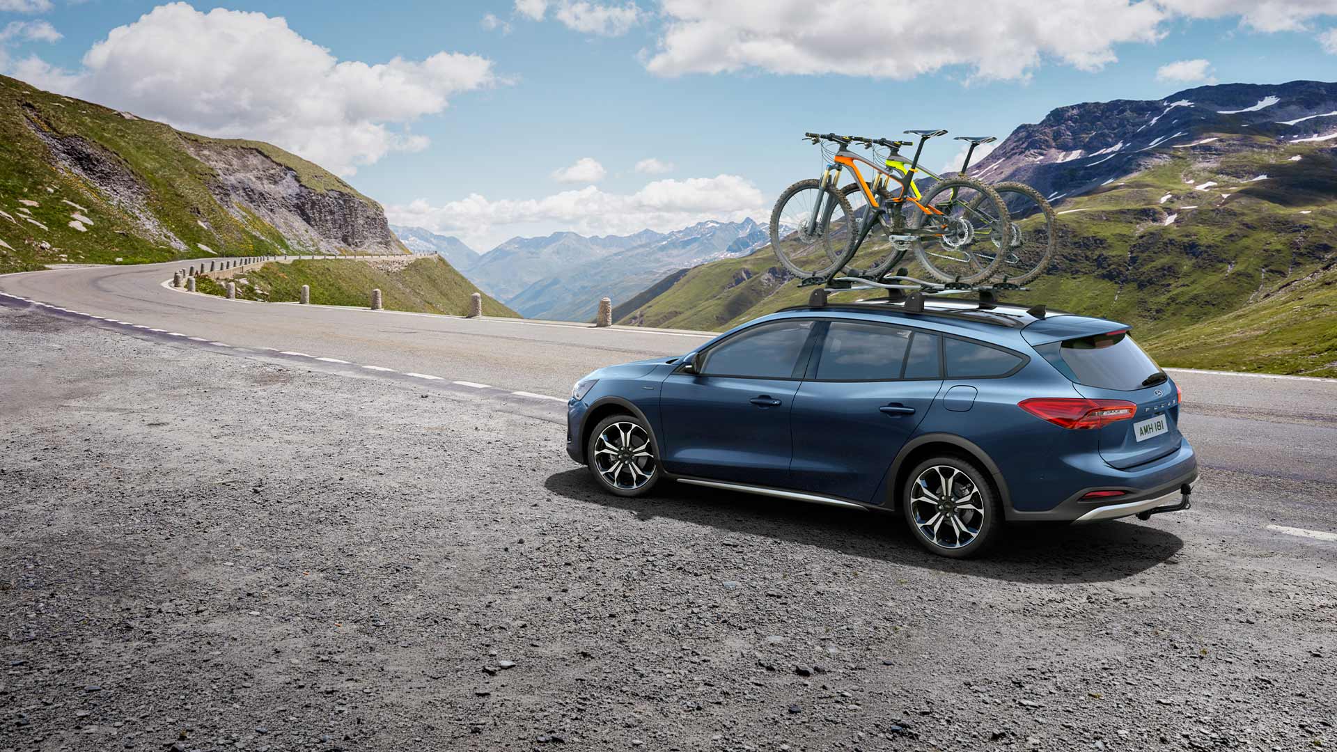Blauwe Ford Focus met fietsen op het dak die op een schilderachtige bergweg rijdt.