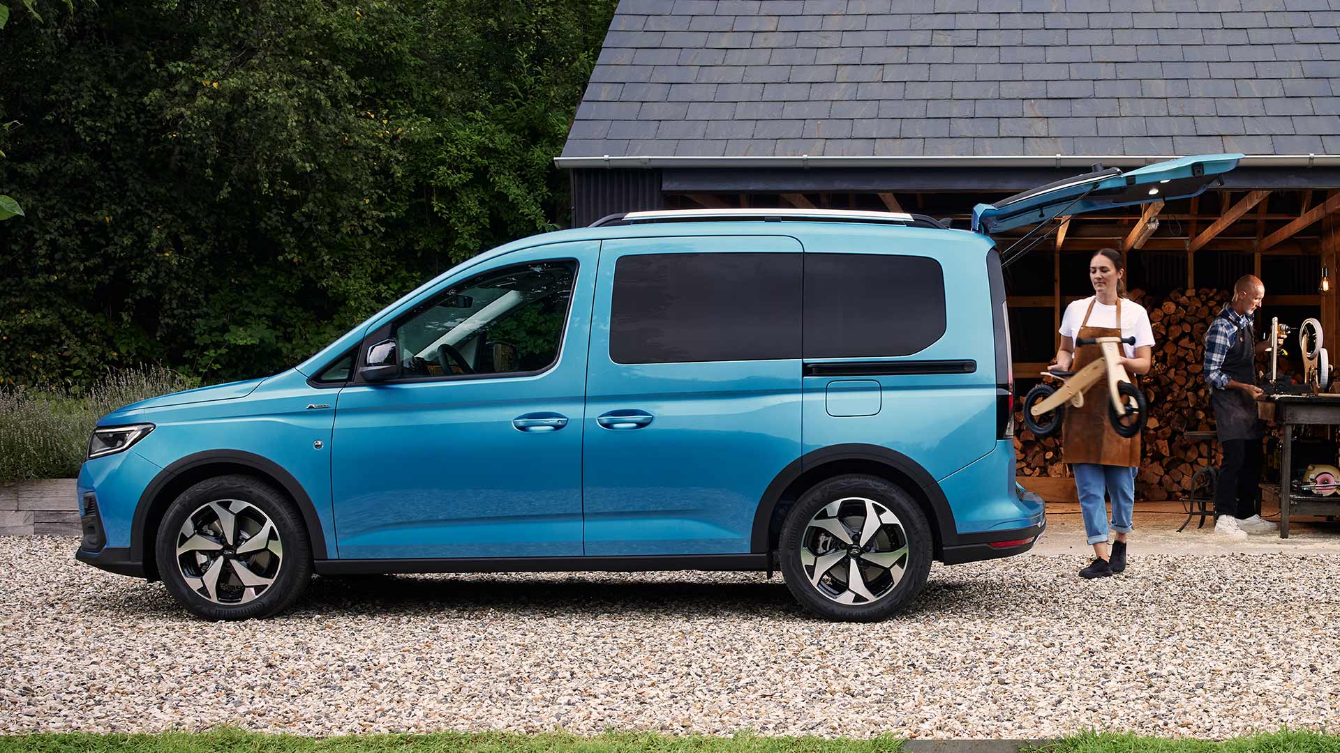 Side view of blue Tourneo Custom with loadspace door open on gravel driveway and a scooter being loaded.