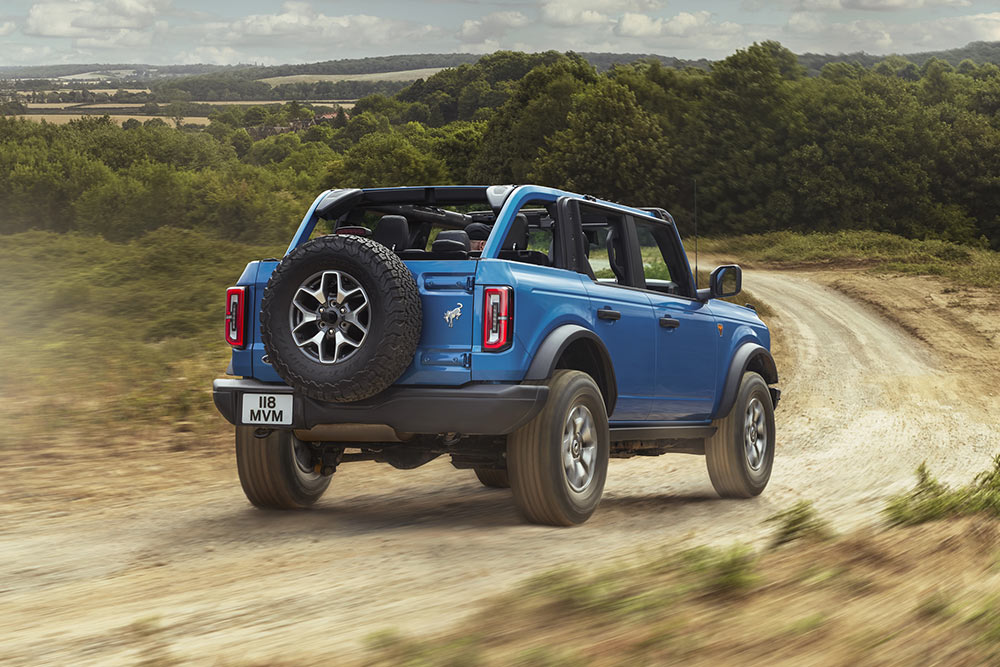 A rear view of a blue Ford Bronco driving through a rural landscape.