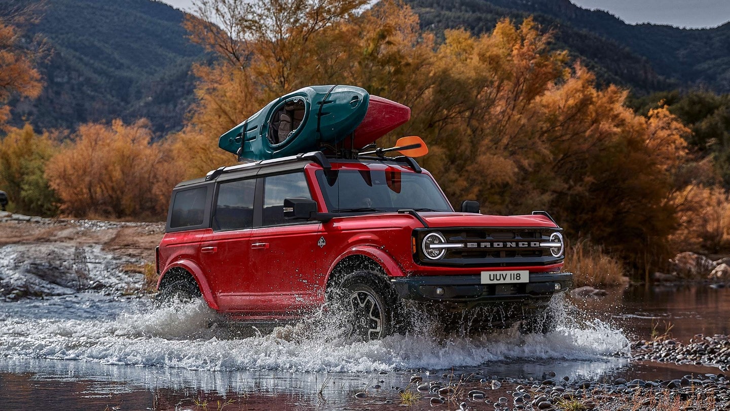 Ford Bronco driving through a small lake in the mountains with kayaks attached to the roof